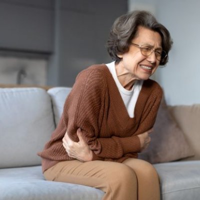 an older woman sits on a sofa clutching her stomach